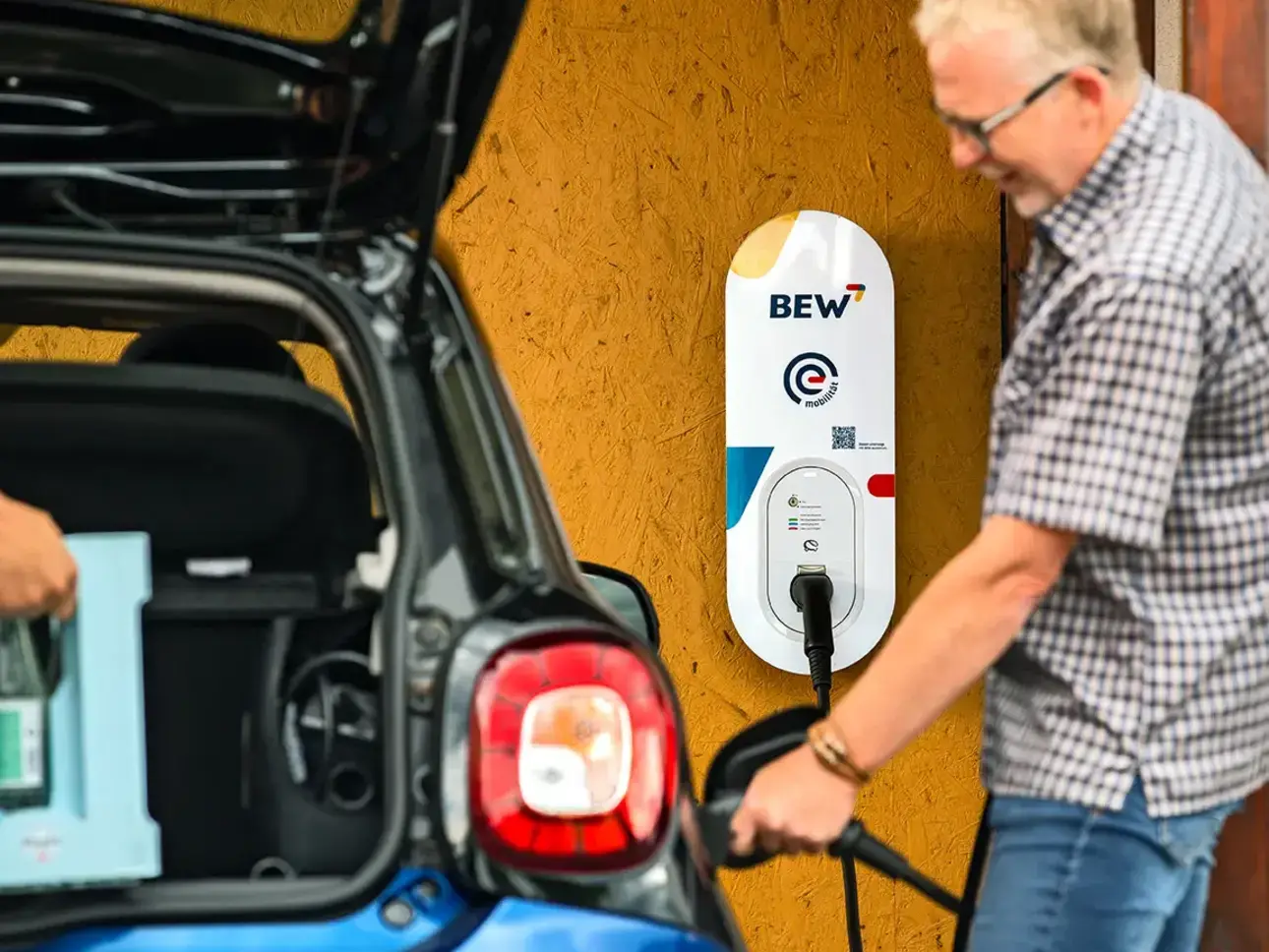 Junger Mann lädt Elektrofahrzeug an einer BEW Wallbox in einer Garage.